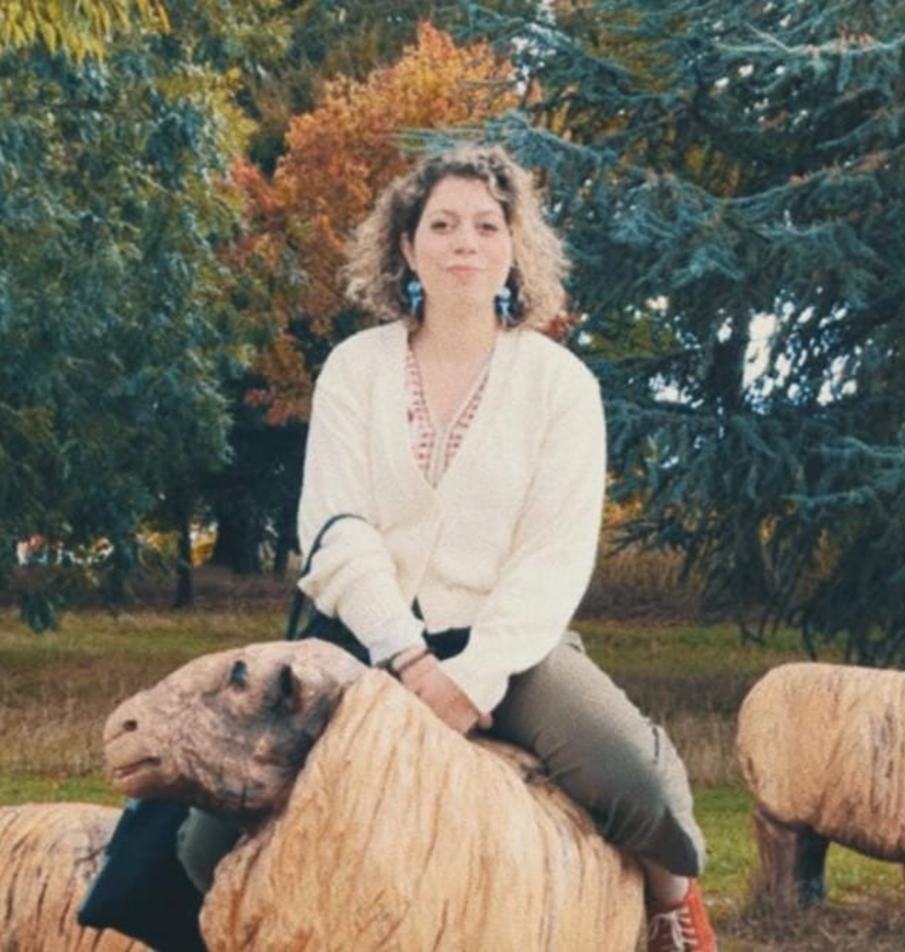 Photo of Marianna looking away while mounting a wooden sheep, in film style